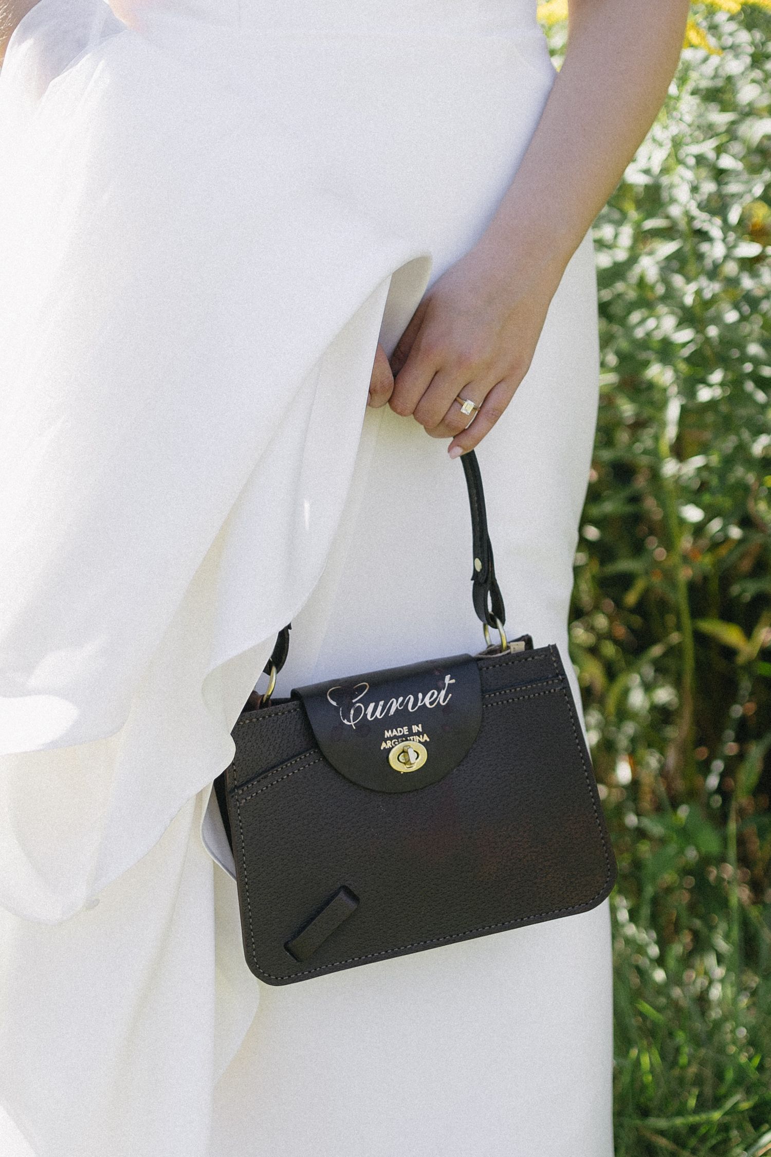 Black handbag with 'Forever' text shown against a white wedding dress outdoors.