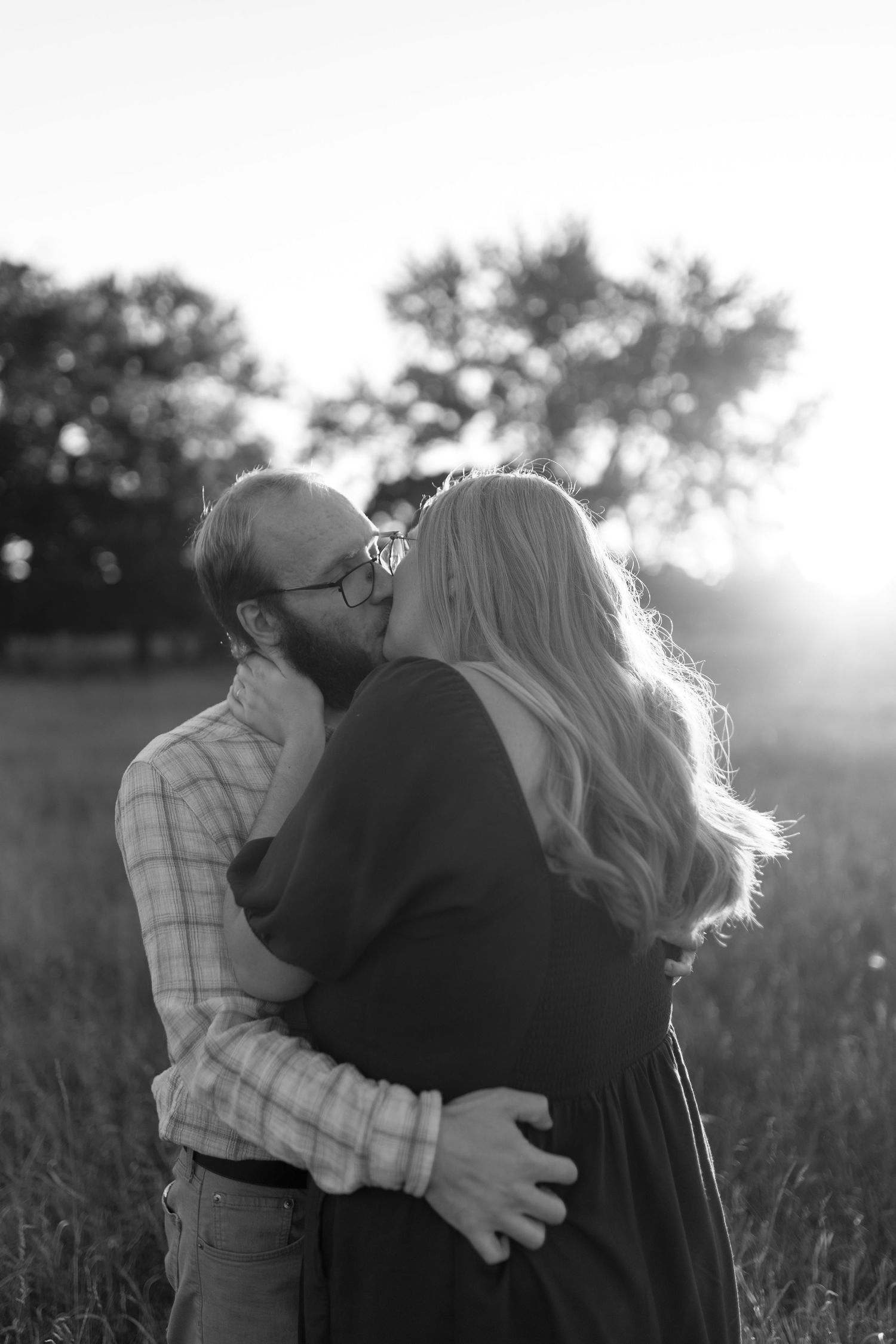 Romantic couple embracing in a sunlit field during golden hour with soft backlighting.