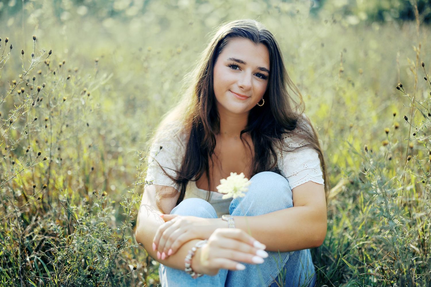 A person in a white top poses outdoors in a sunny field of yellow wildflowers for a series of candid shots.