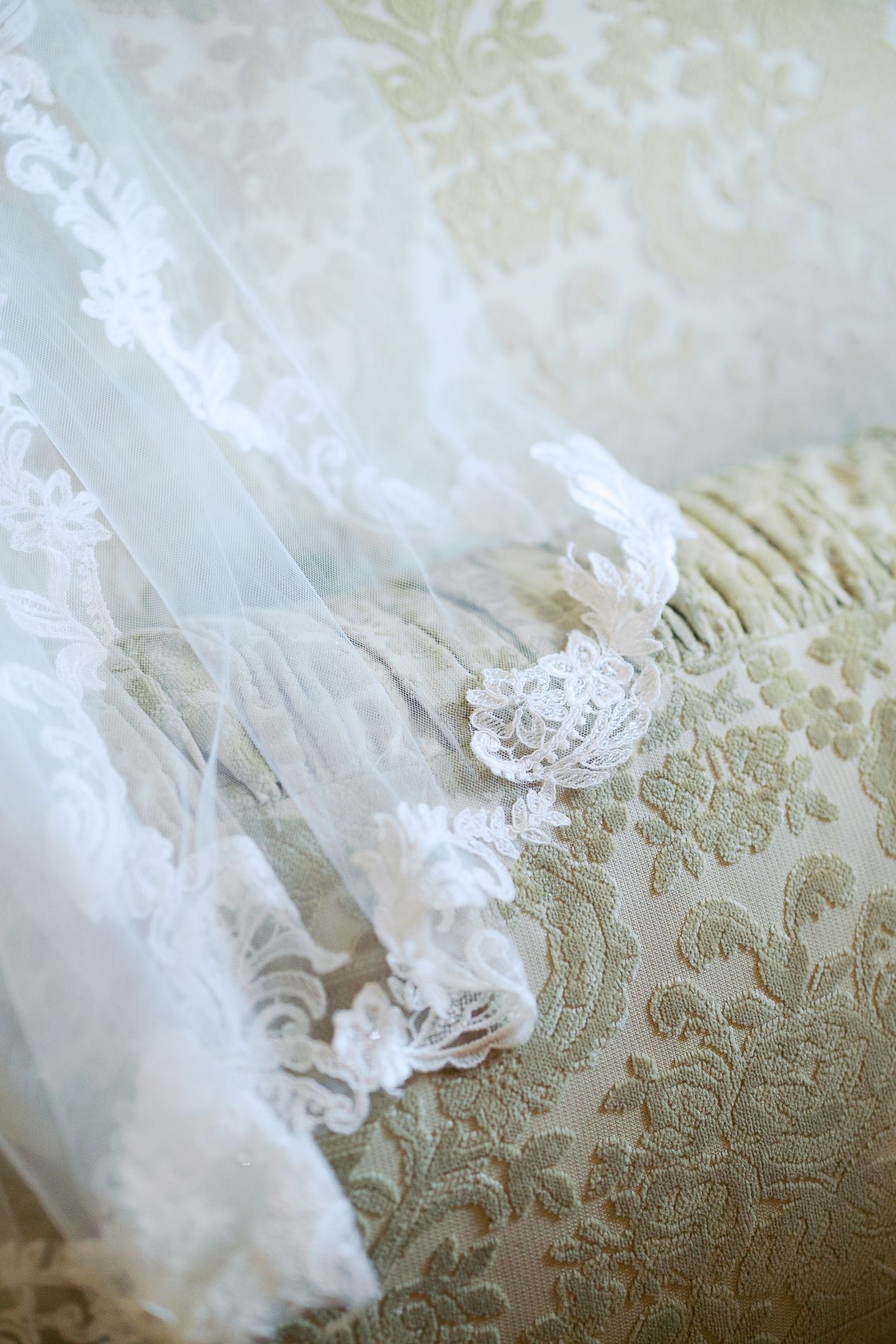 Delicate white lace and tulle fabric details resting on an ornate damask upholstery with floral patterns.