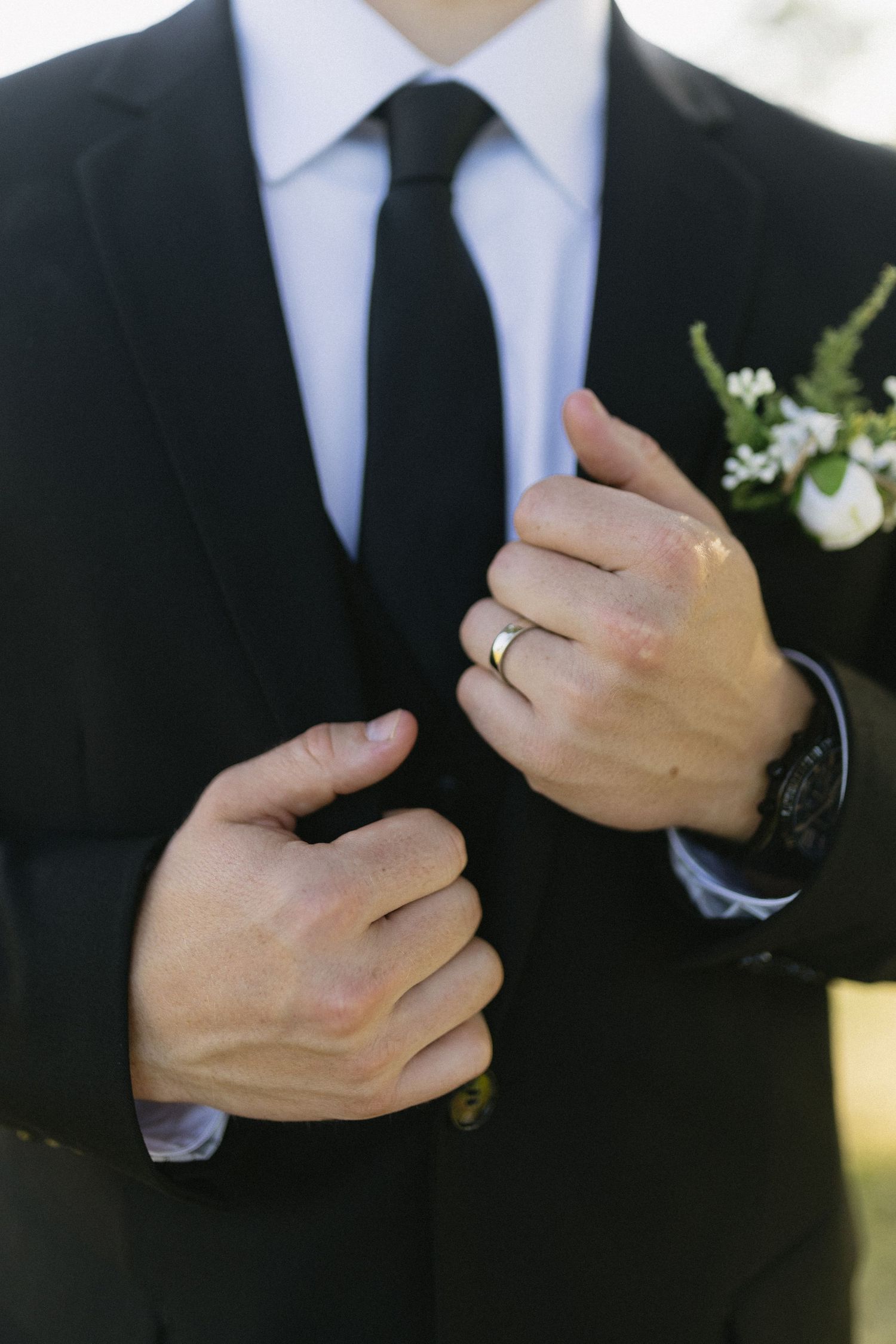 Close-up of groom's formal suit with boutonniere and wedding ring.