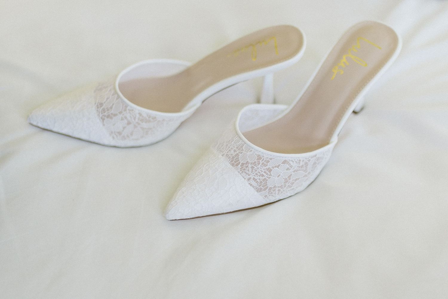 Elegant white lace pointed-toe mule wedding shoes displayed on light fabric.