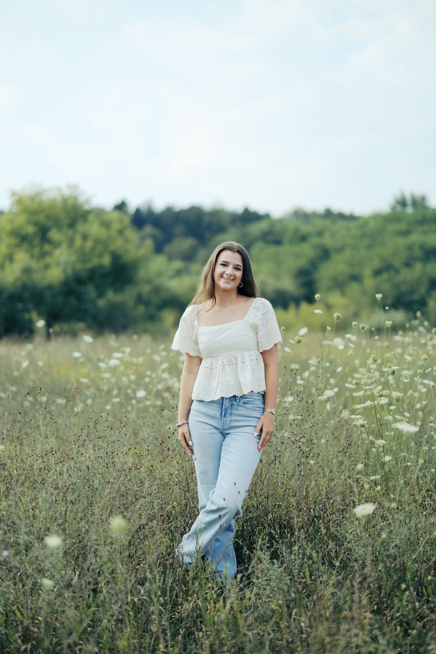 A person in light blue jeans and white top stands in a sunny wildflower meadow during summer.