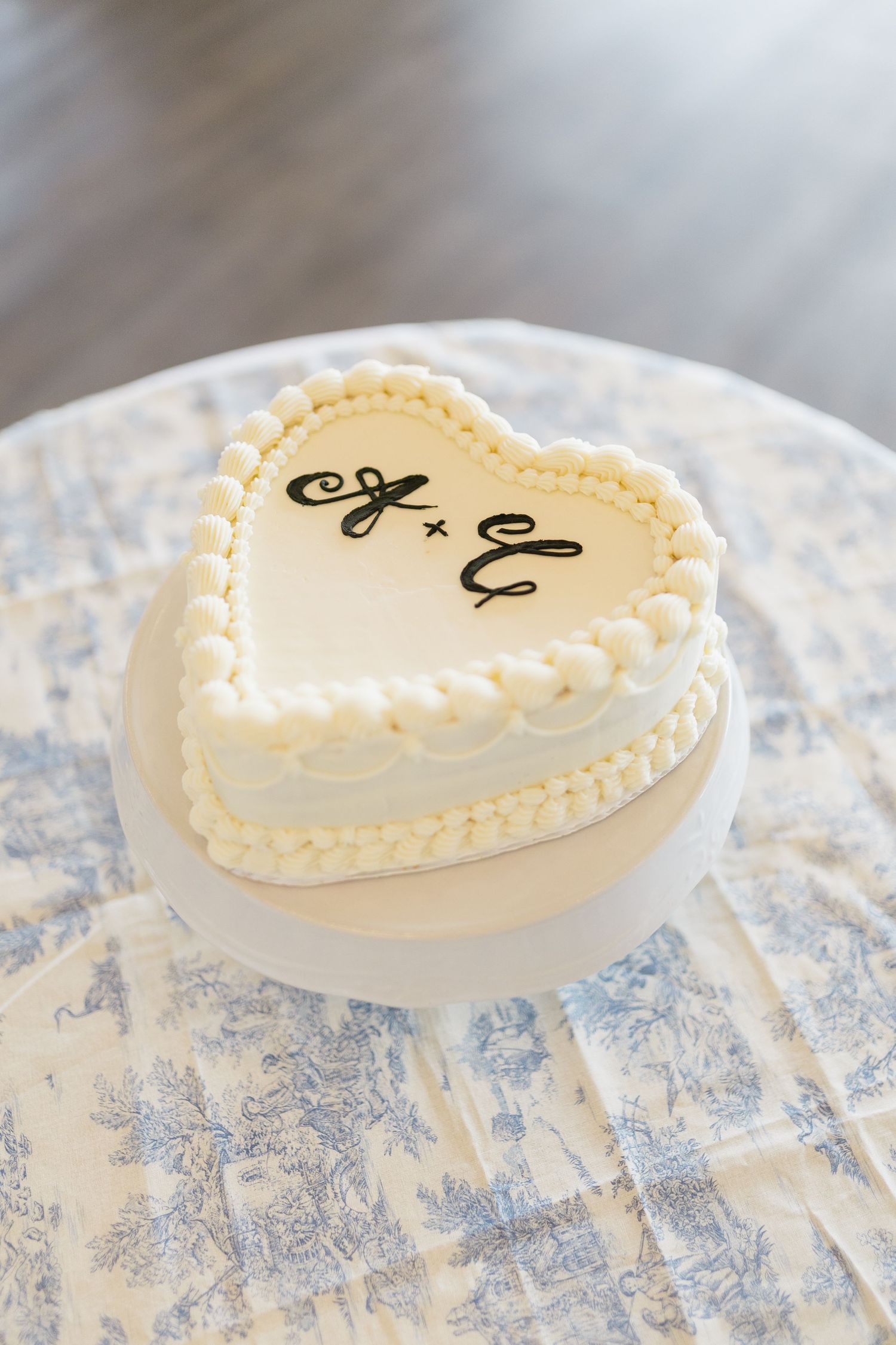 Heart-shaped wedding cake decorated in white frosting with monogram initials and pearl border.