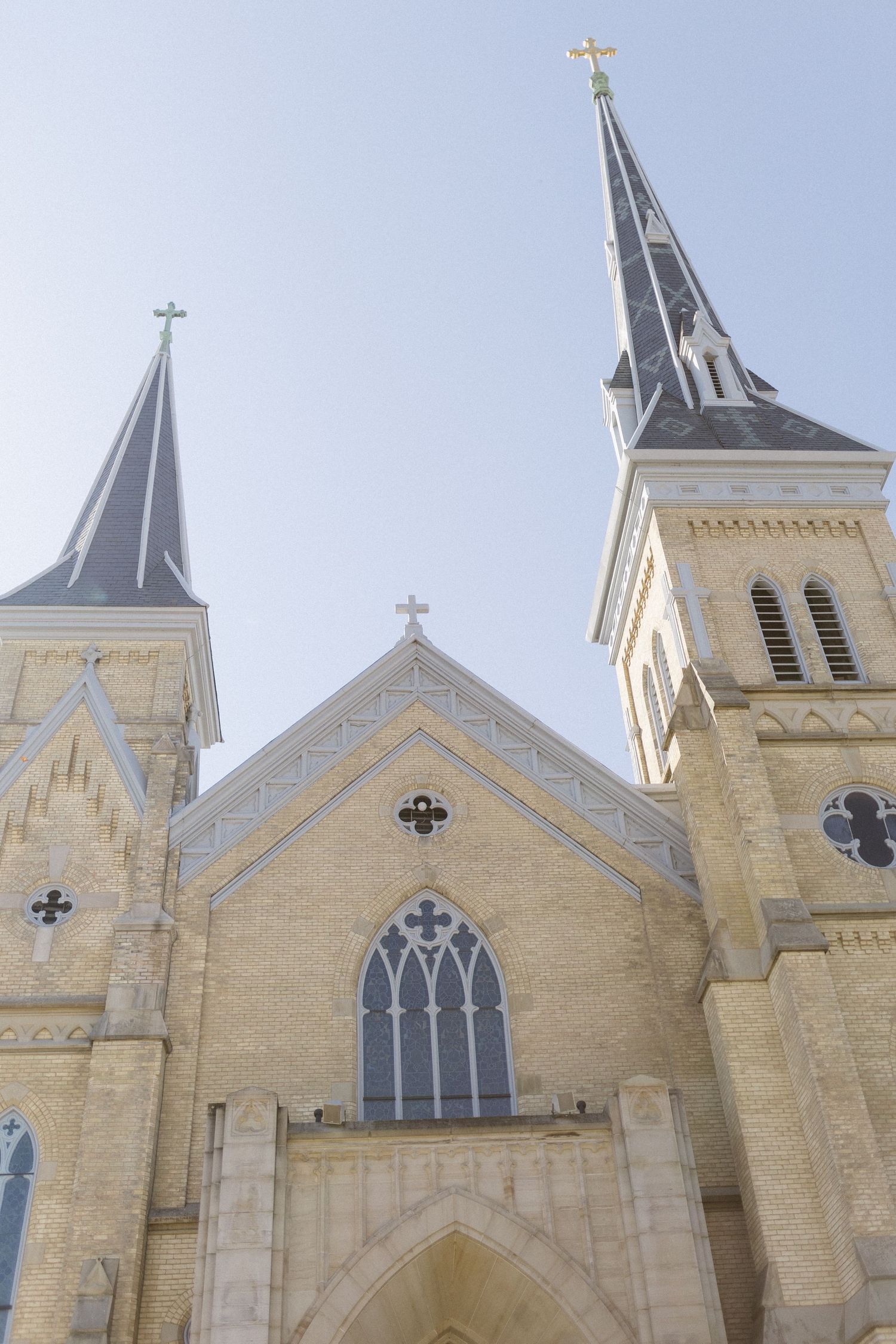 Two Gothic church steeples rise against a light sky, showcasing beige stone architecture with arched windows and cross details.