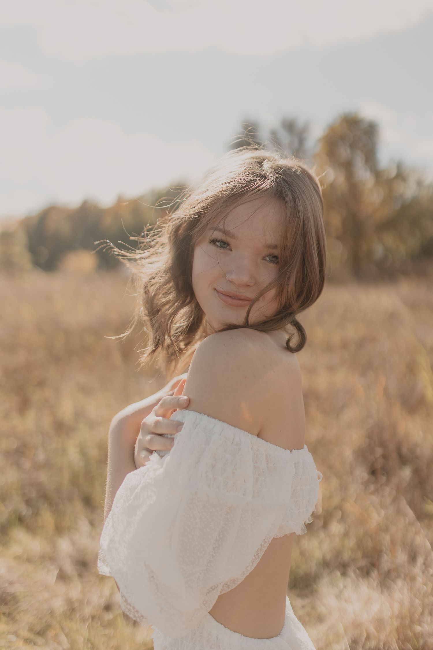 Portrait of woman in white off-shoulder dress in golden field during sunset.