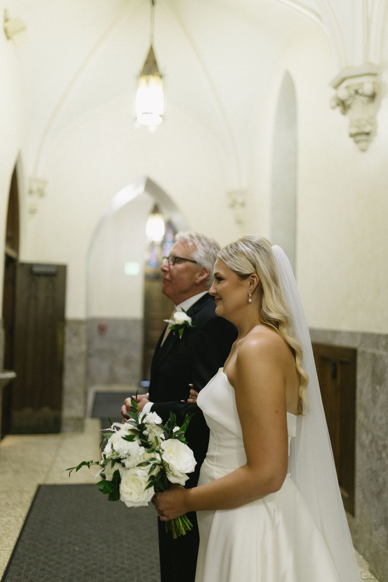 A pair standing in a church hallway with white flowers during a wedding ceremony.