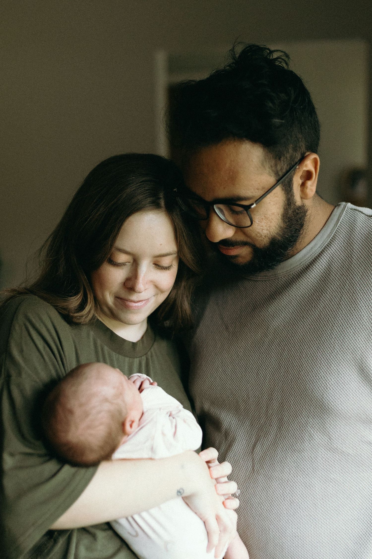 A couple shares an intimate moment with their newborn baby in a dimly lit room.