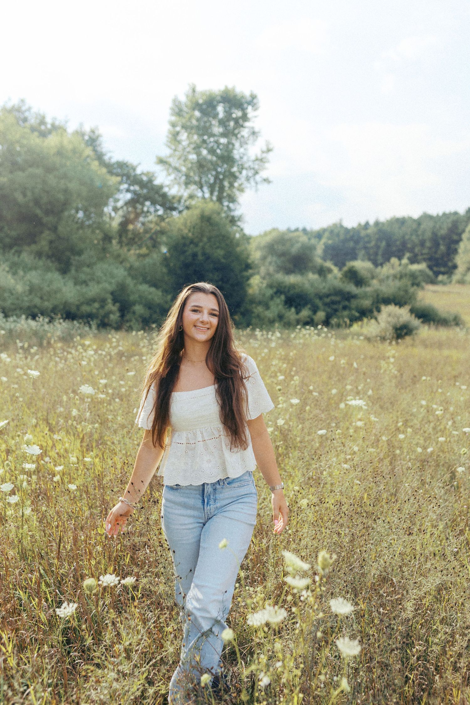 A person stands in a sunny wildflower meadow wearing a white top and light blue jeans on a summer day.