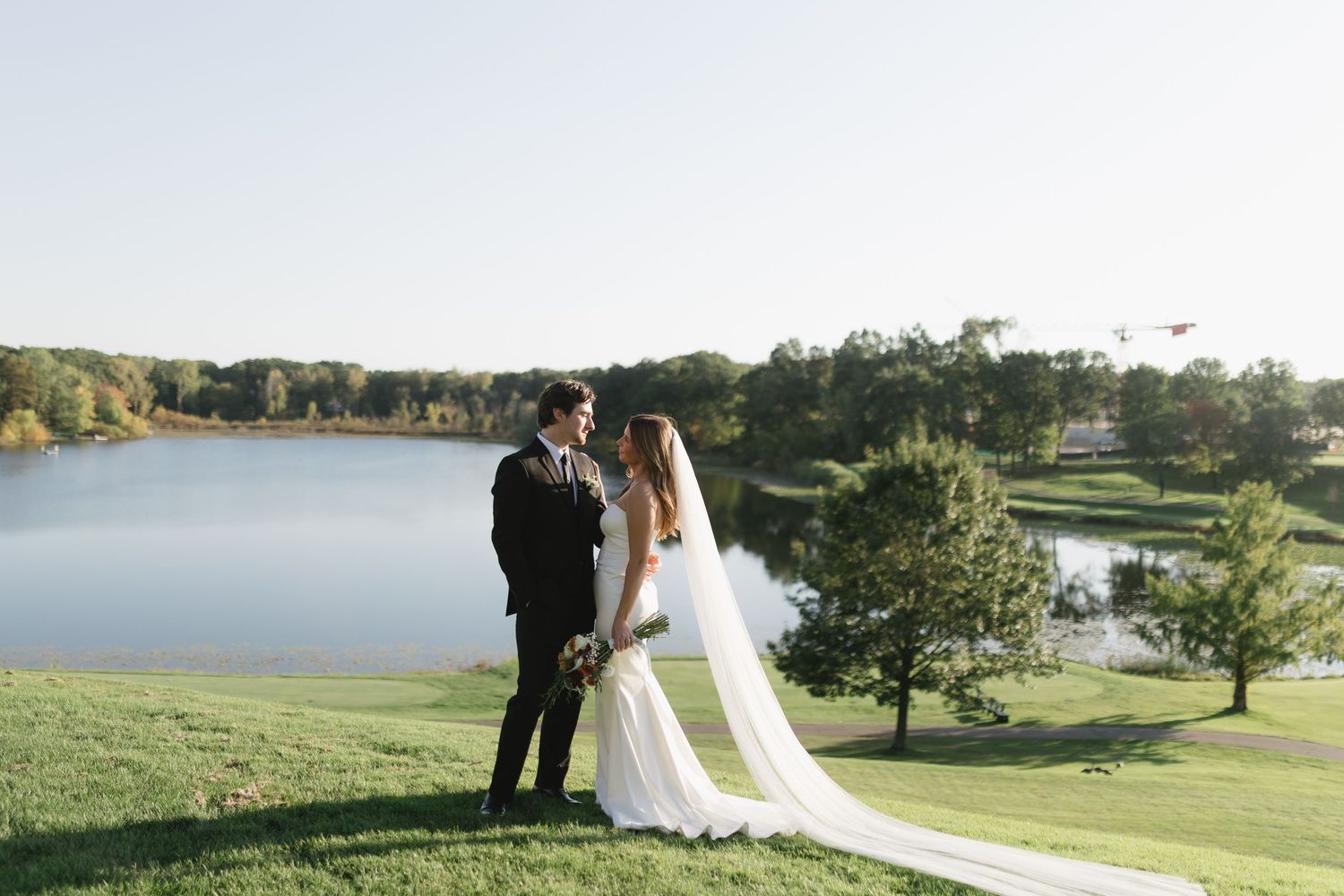 Scenic wedding photograph overlooking a lake with couple standing on a grassy hillside.