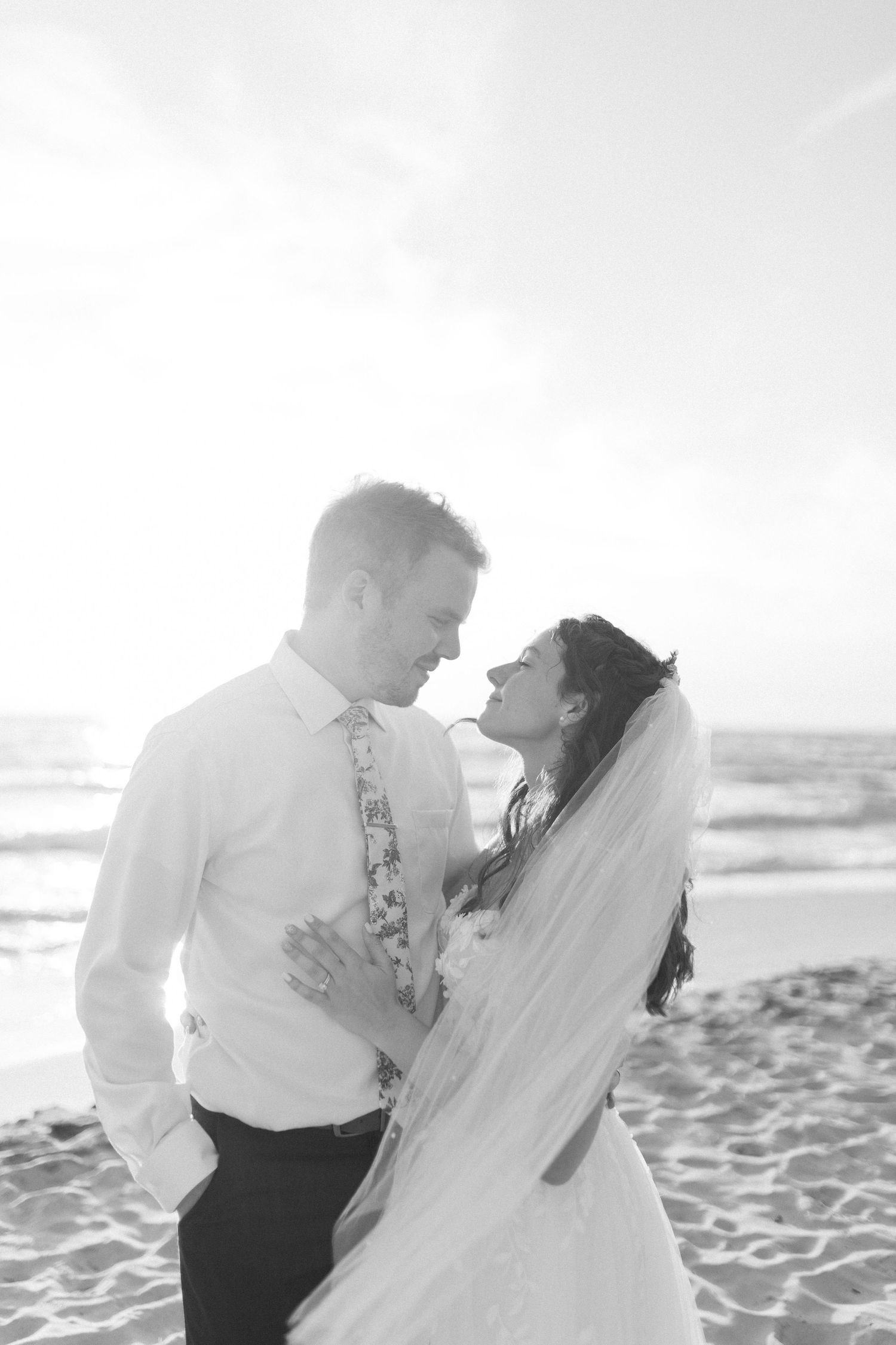 A black and white portrait of newlyweds sharing an intimate moment on a beach.