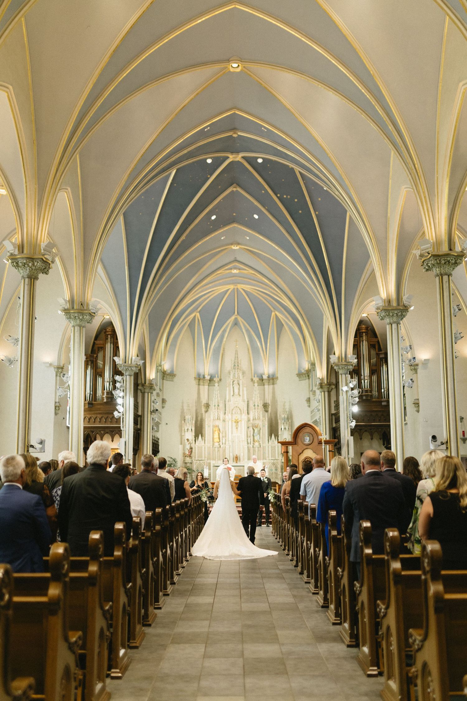 Cathedral interior with vaulted ceiling and rows of pews during a wedding ceremony.