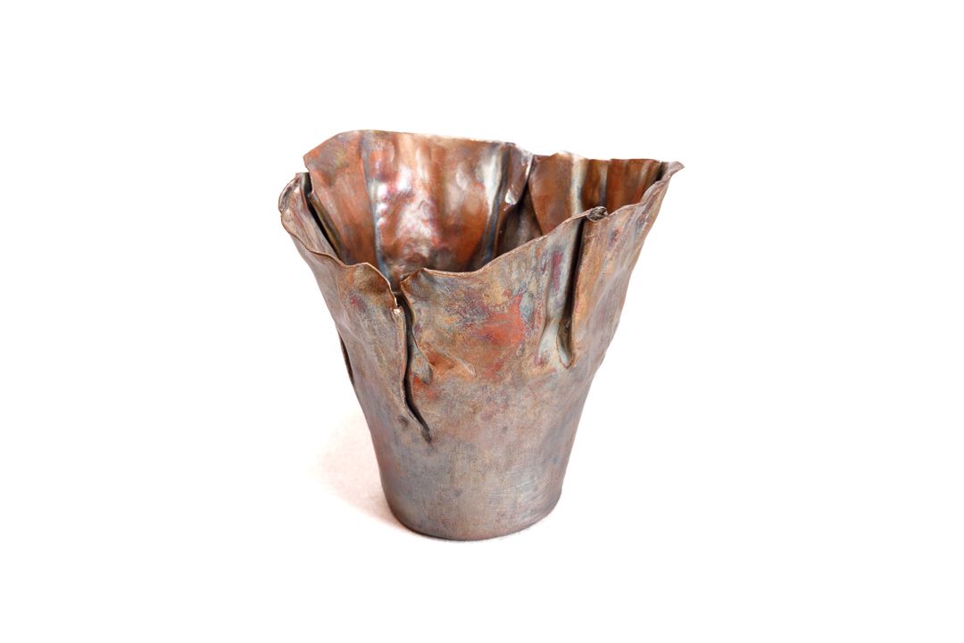 A hand formed cone shape copper vessel with wrinkle surface texture near the lip.