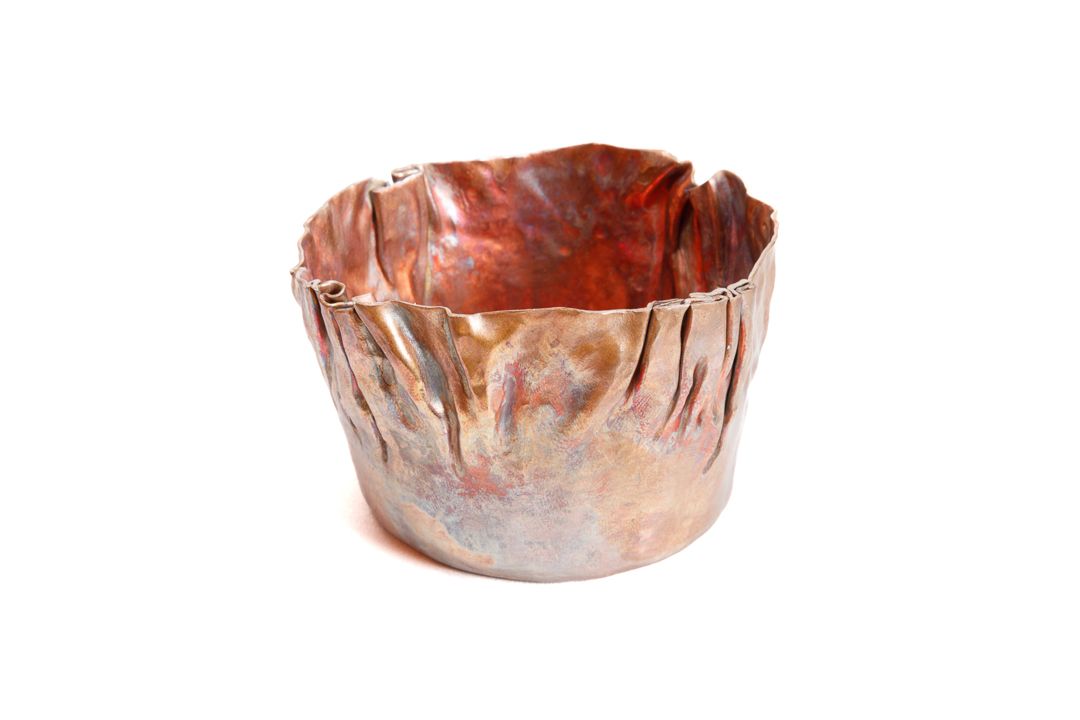 A hand formed  round copper vessel with wrinkle surface texture near the lip.