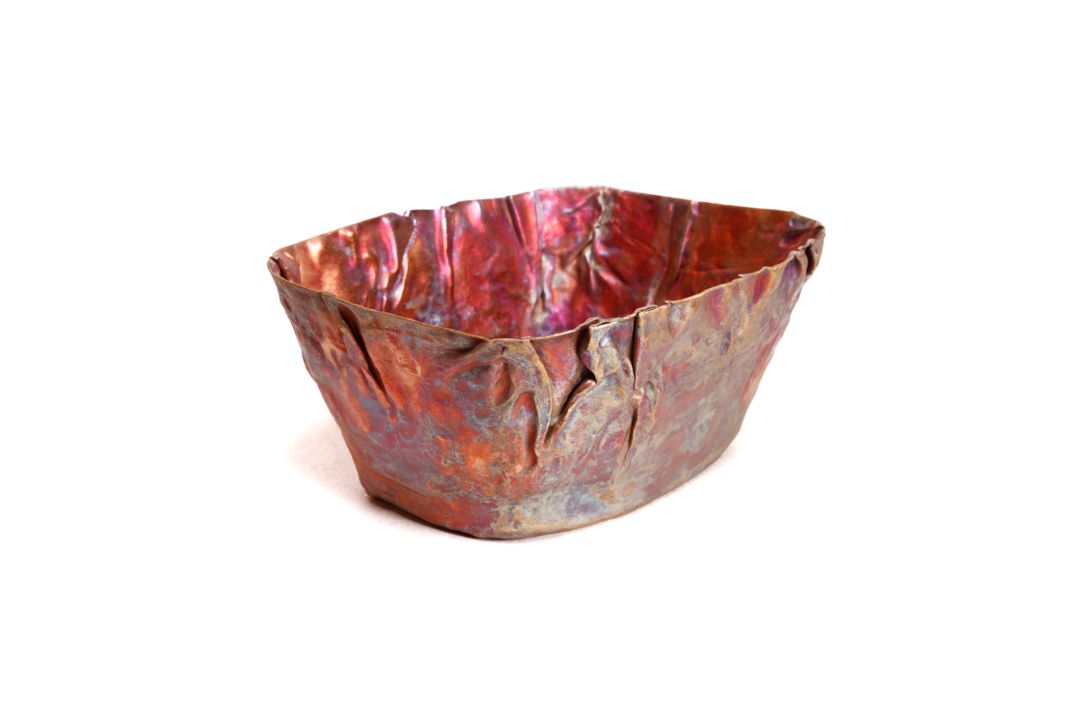 A hand formed copper vessel with wrinkle surface texture near the lip and a rectangular shape.