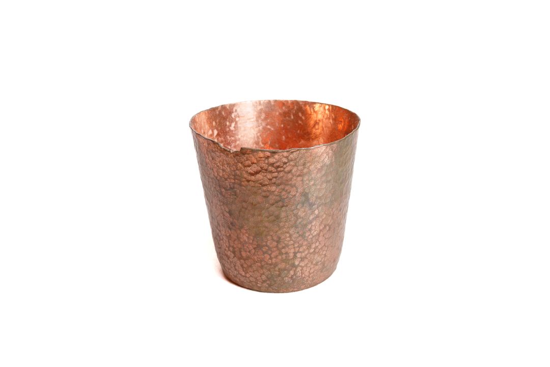 A small hand formed copper cup shaped vessel, with a dimple like surface texture.