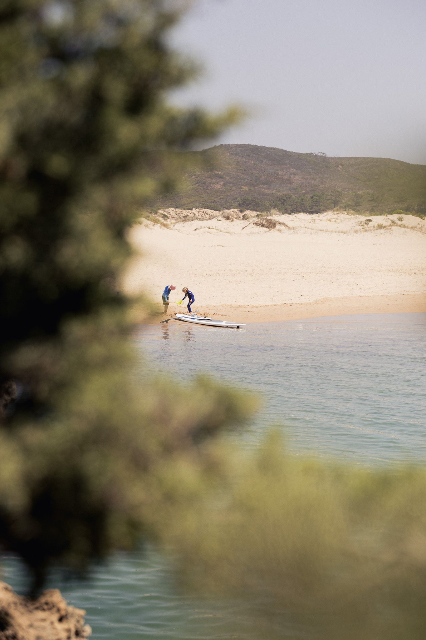 Deux personnes avec un paddle sur une plage de sable encadrée d'arbres verts