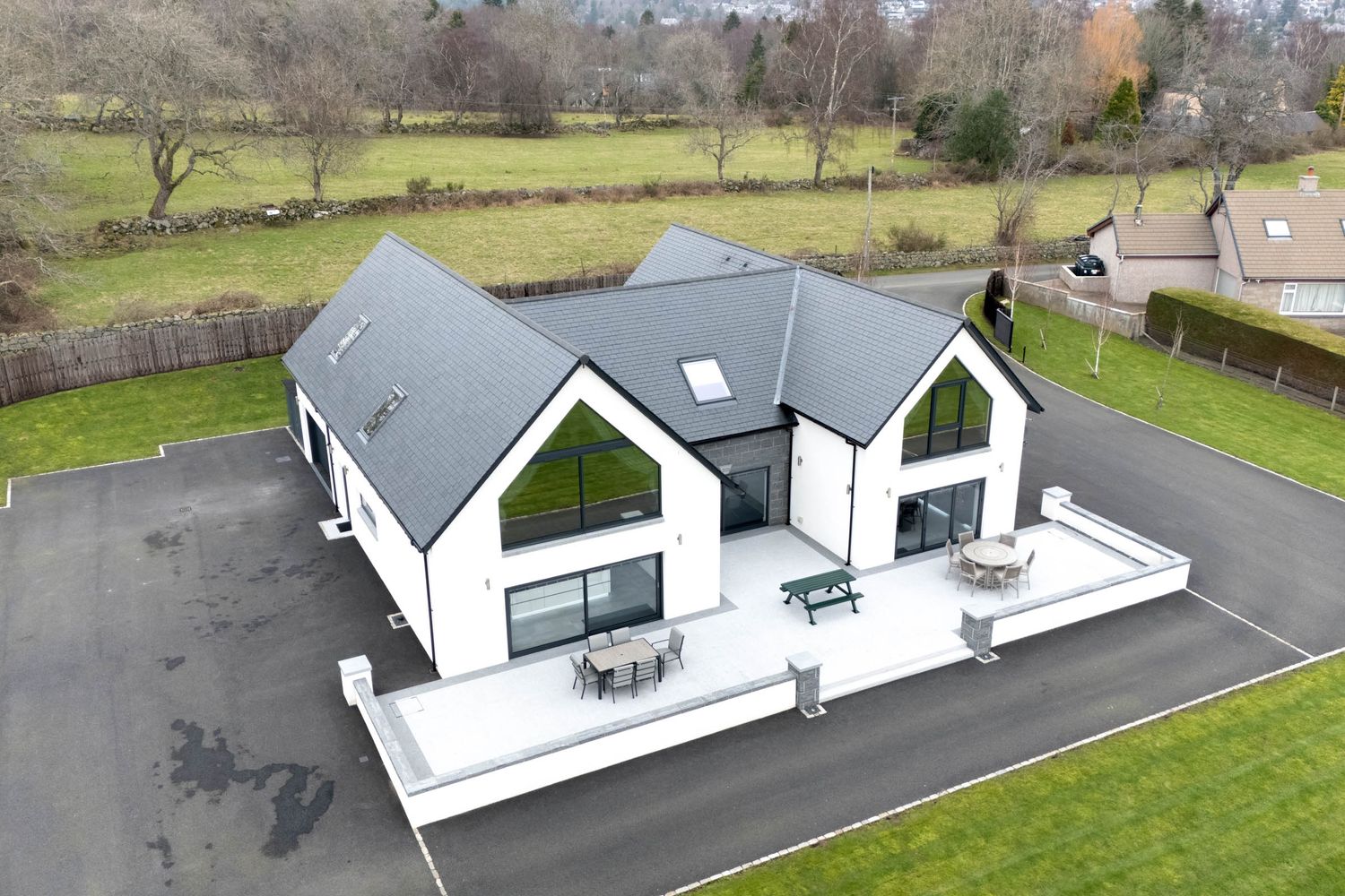 Modern white and gray house with large windows and patio areas viewed from above by drone camera.