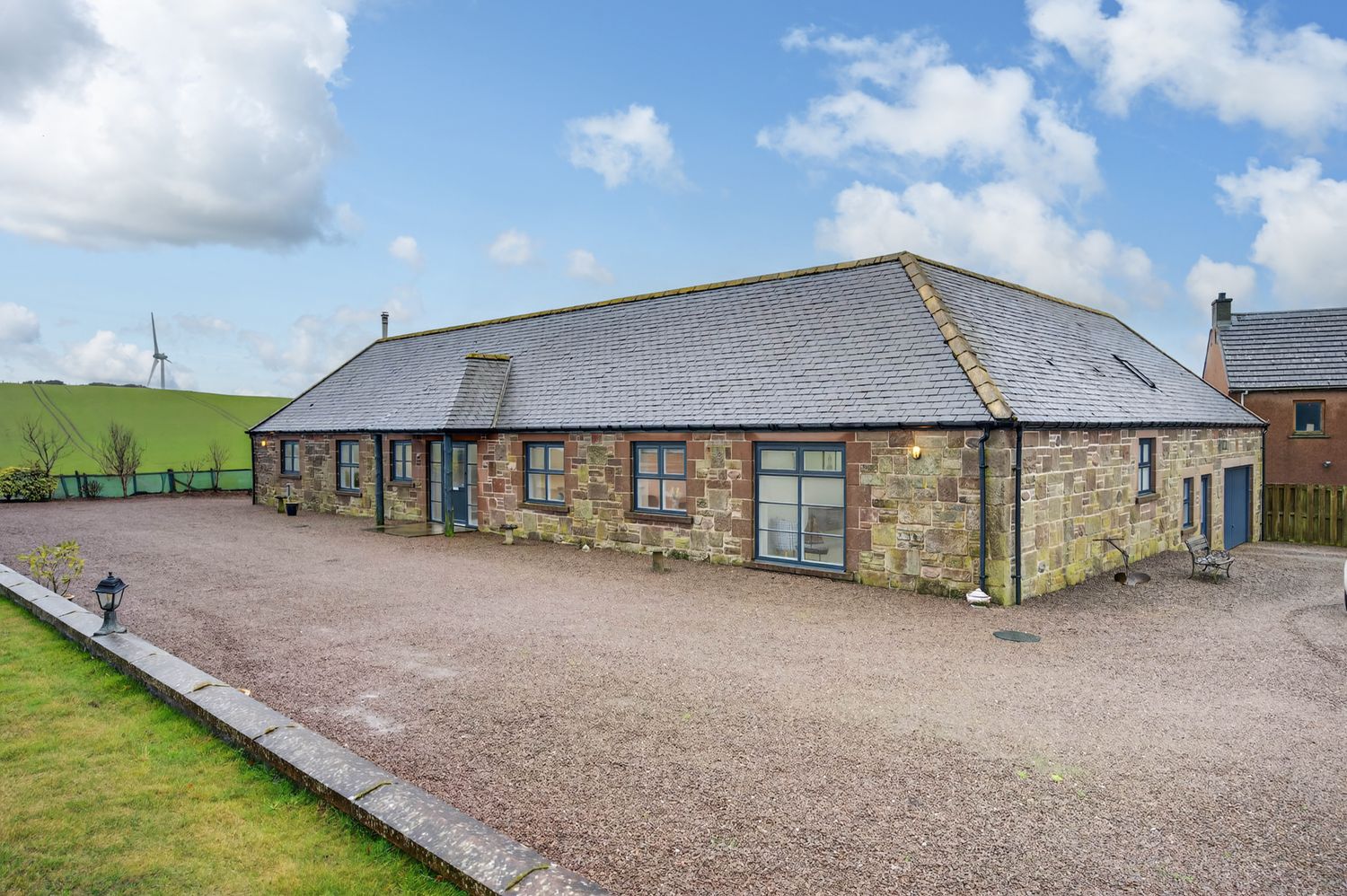 Long converted stone barn building with gravel driveway and modern glass doors.