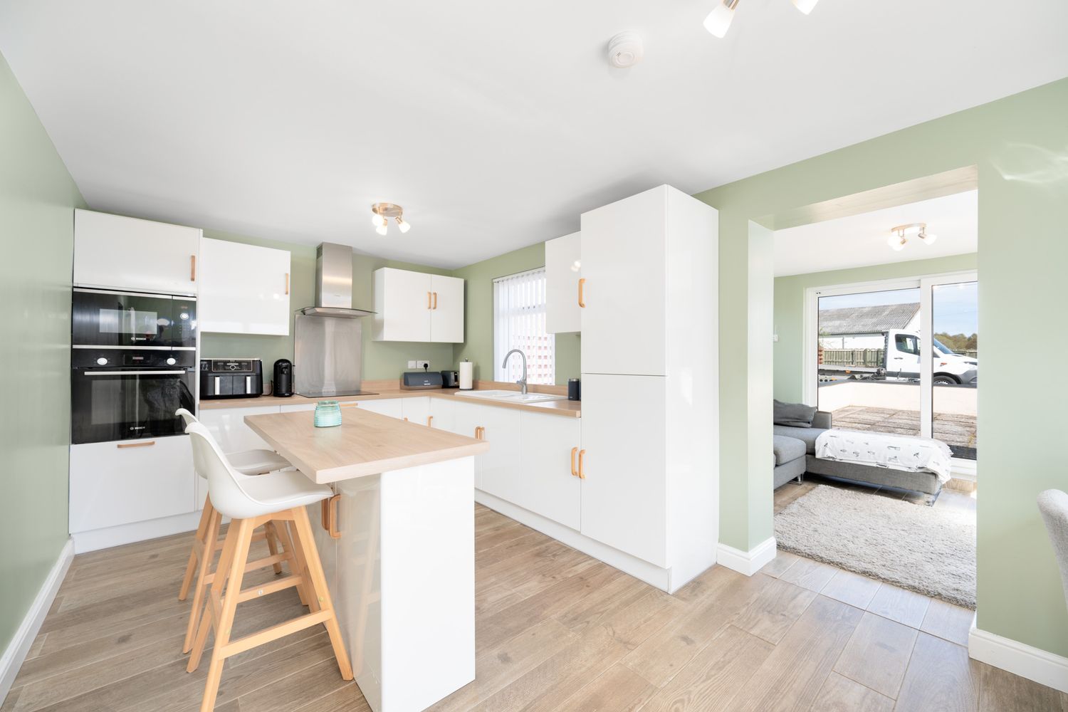 Modern white kitchen with wooden floors, integrated appliances, and a breakfast bar island featuring mint green walls.