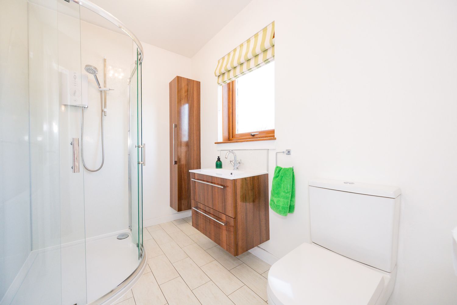 Modern bathroom interior with glass shower enclosure, floating wood vanity, and beige tile flooring in bright natural light.