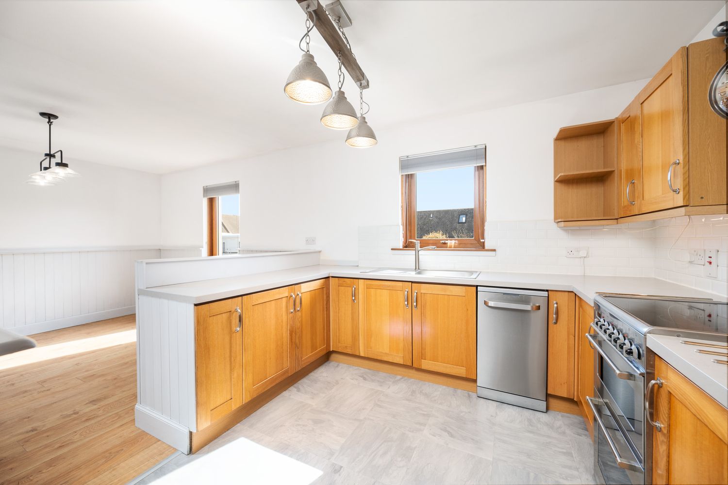 Modern kitchen features honey oak cabinets, stainless appliances, and track lighting in an L-shaped layout with natural light.