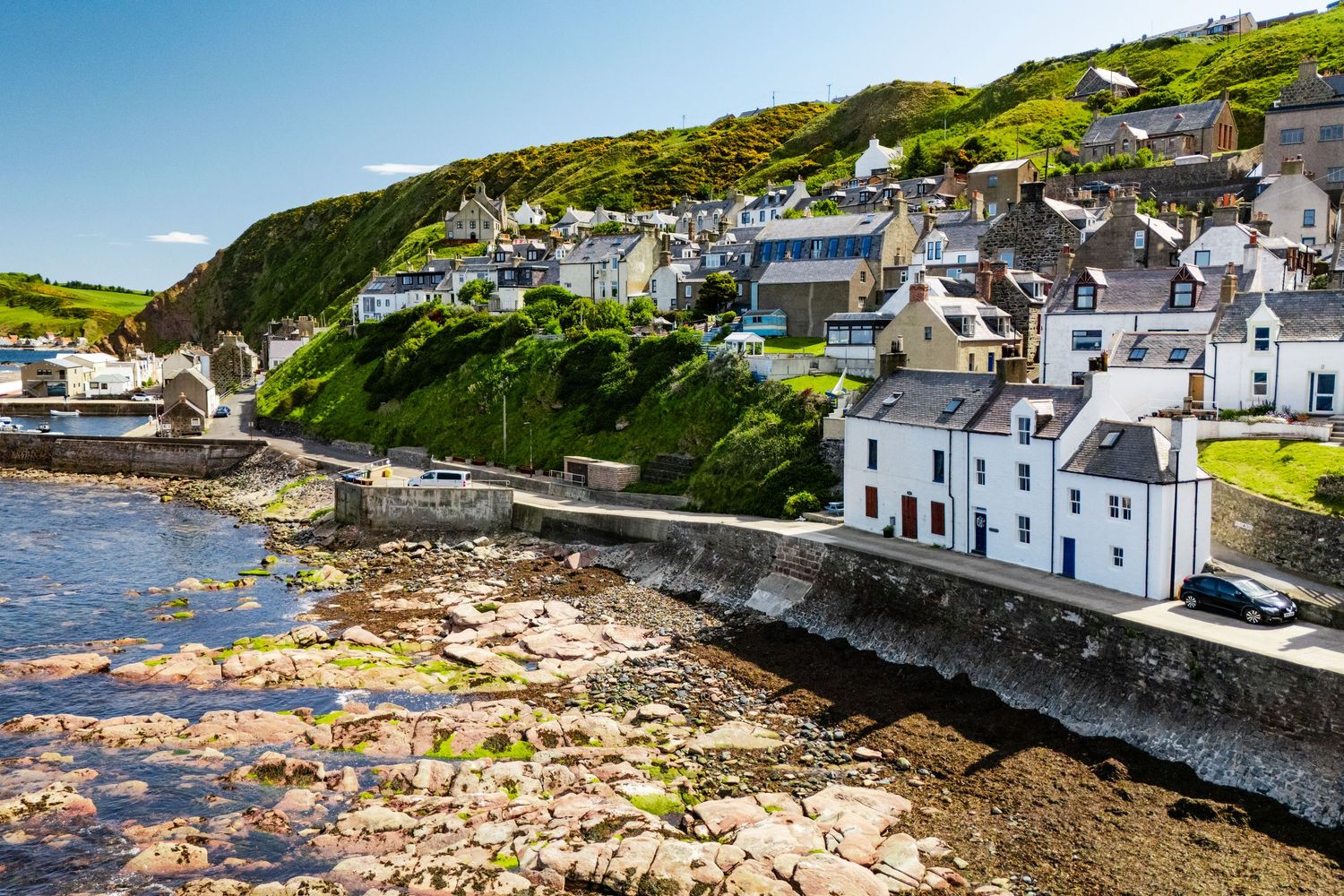 Picturesque seaside village with white buildings along curved stone wall and rocky coastline.