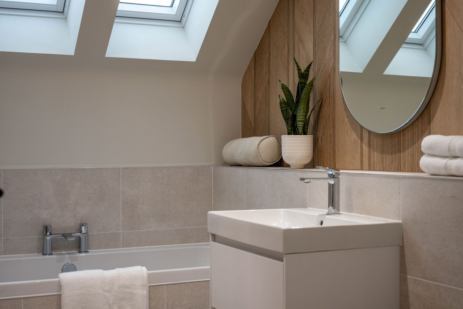 Contemporary bathroom with skylight windows, wooden accent wall, and floating vanity in neutral tones.