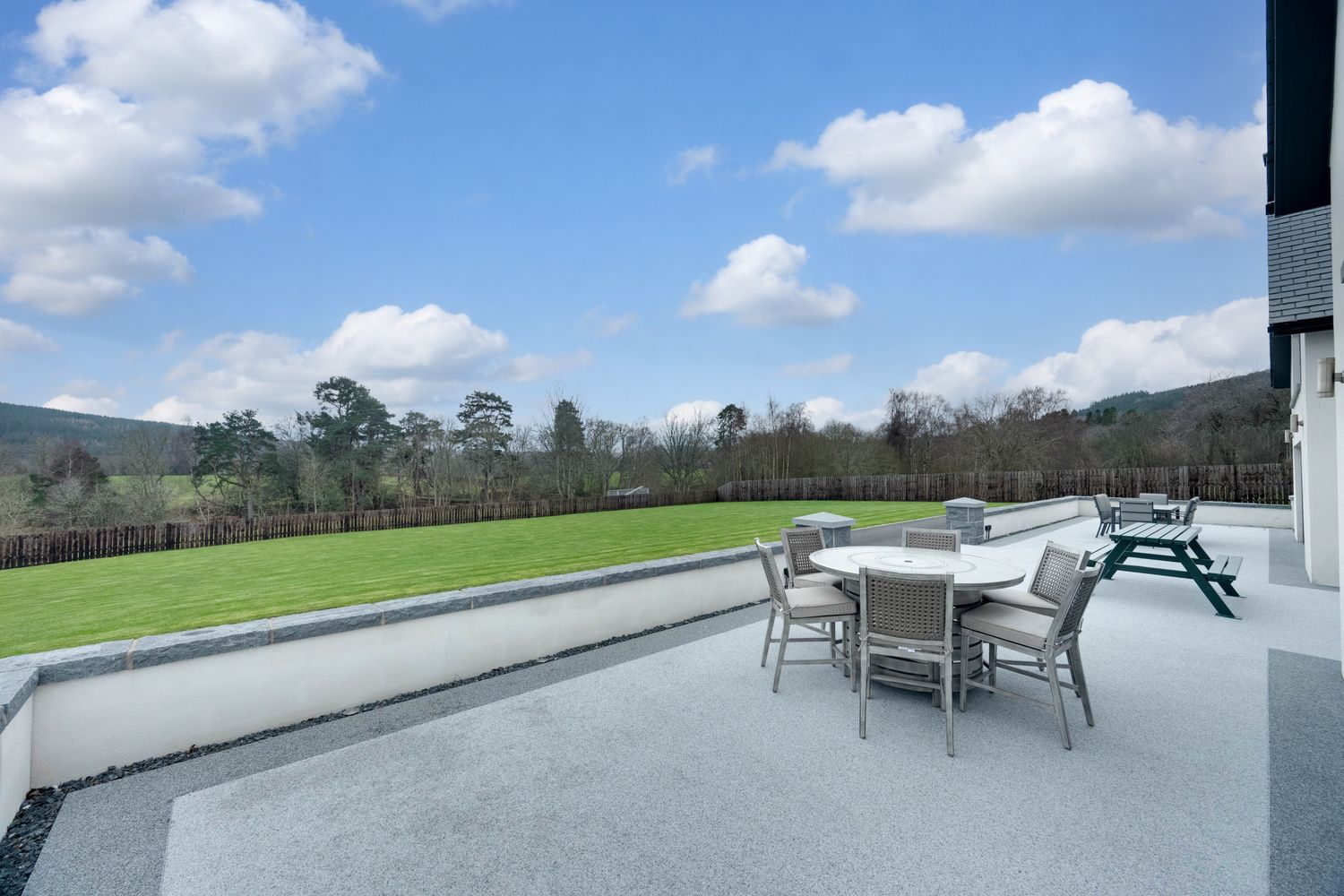 Panoramic view of a modern outdoor terrace with lounge furniture overlooking green rolling hills and mountains.
