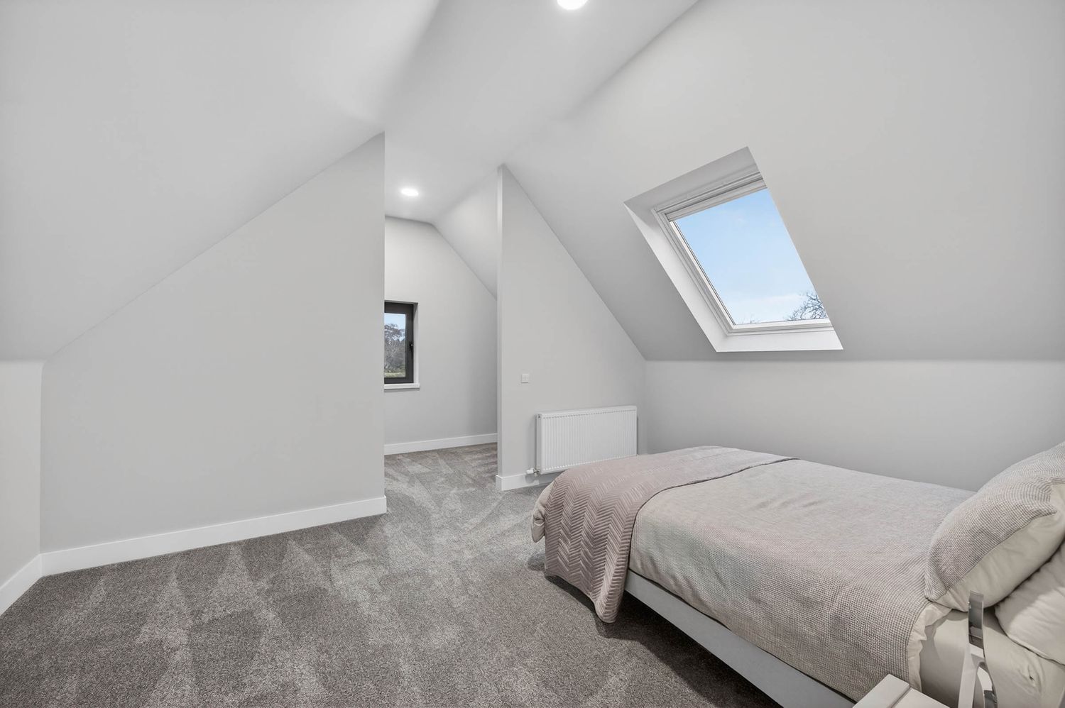 Modern minimalist bedroom interior with white walls, skylights, and built-in storage in a loft conversion.