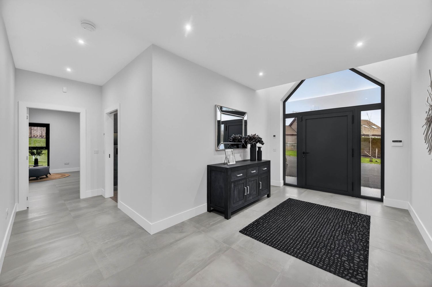 Modern home entryway with gray tile floors, white walls, and black accent cabinet beneath an arched window.