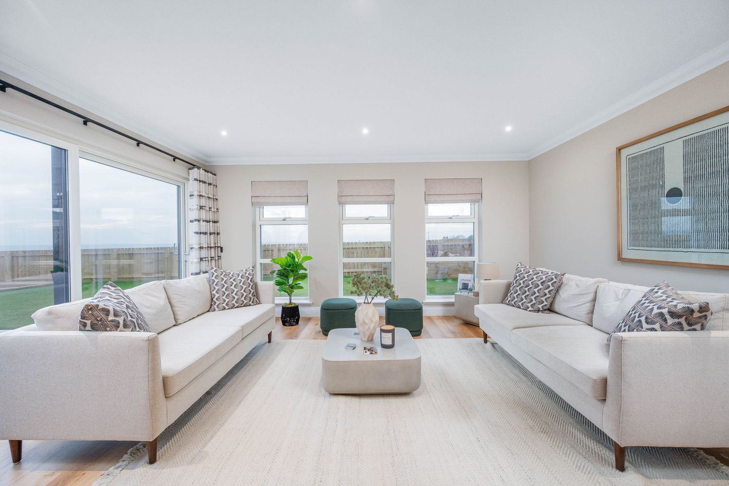 Bright coastal living room with two matching cream sofas and panoramic windows with ocean views.