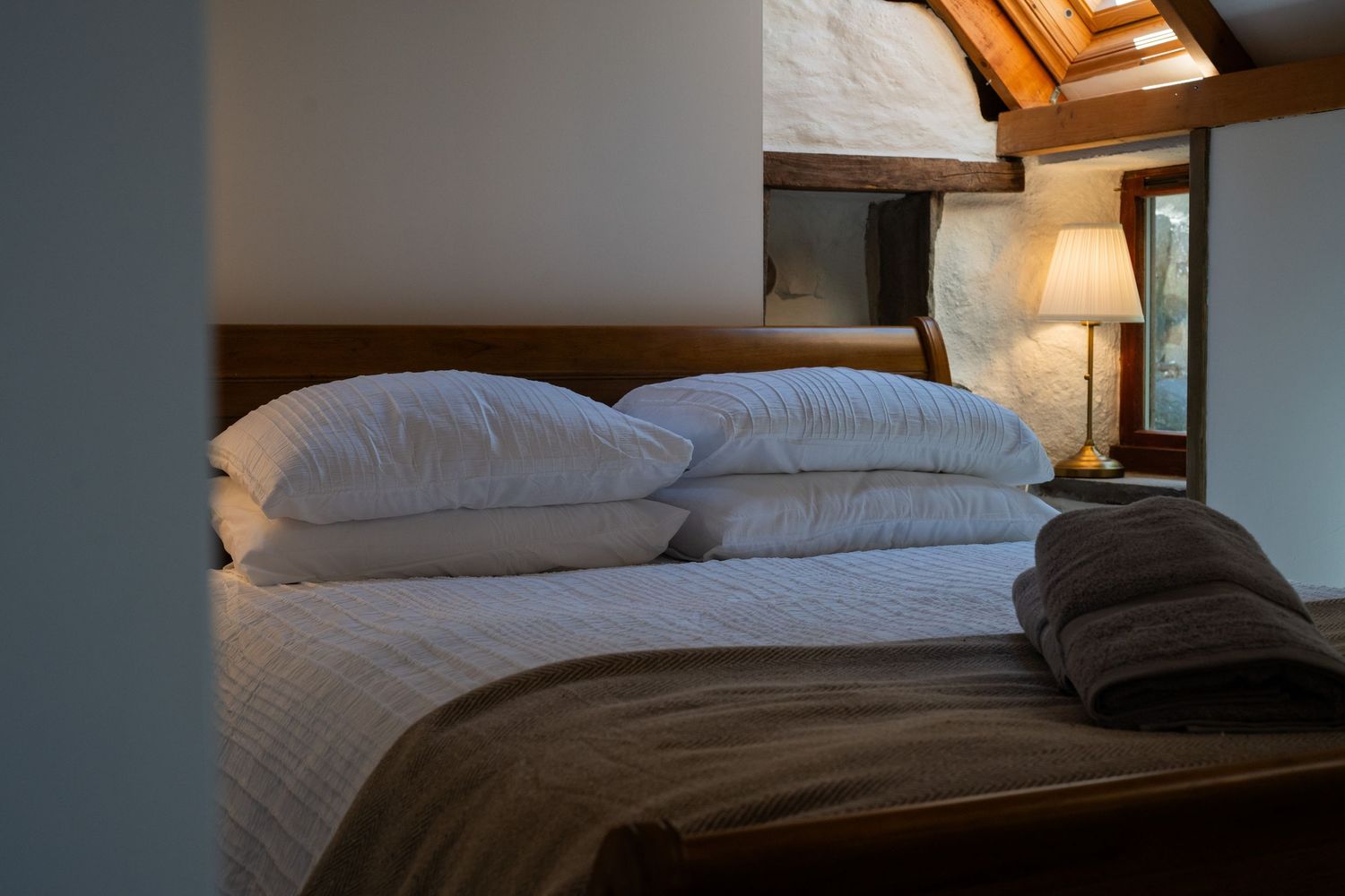 Cozy bedroom interior with stacked white pillows and brown comforter on bed beneath warm lighting.