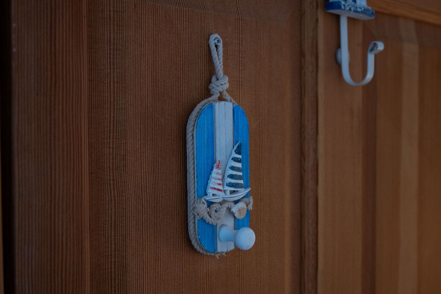 Decorative blue and white wooden buoy with sailboat design hanging on wall hook.