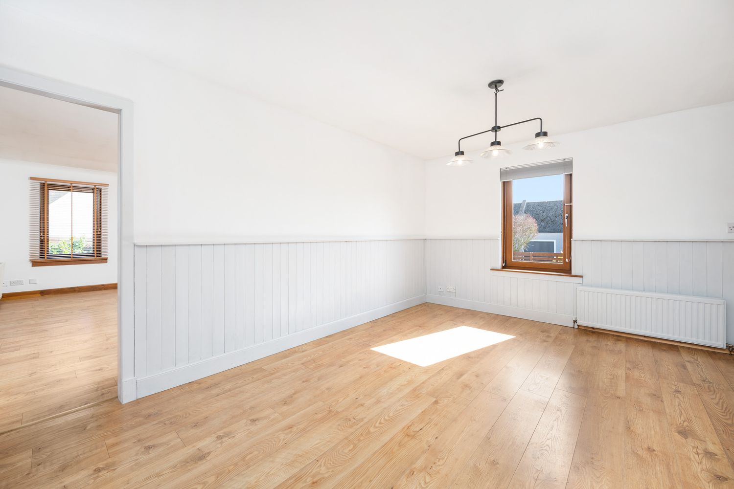 Empty living room with hardwood floors, white wainscoting, wood trim windows and track lighting fixture.