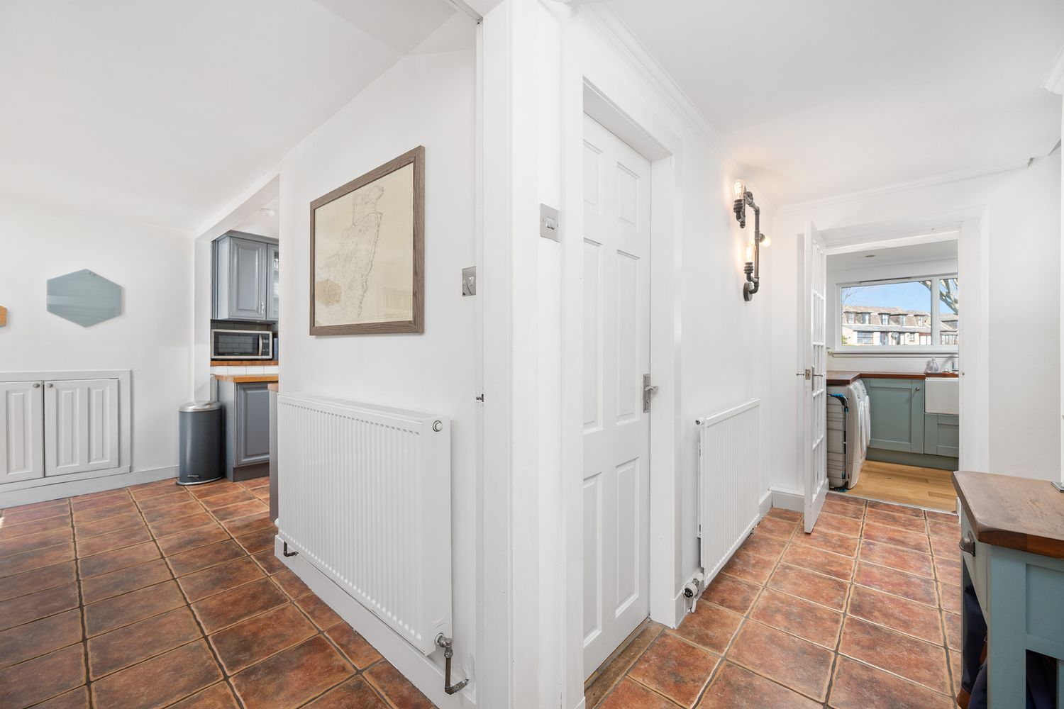 Interior view of hallway with terracotta tile floors, white walls and built-in storage showing connecting rooms.
