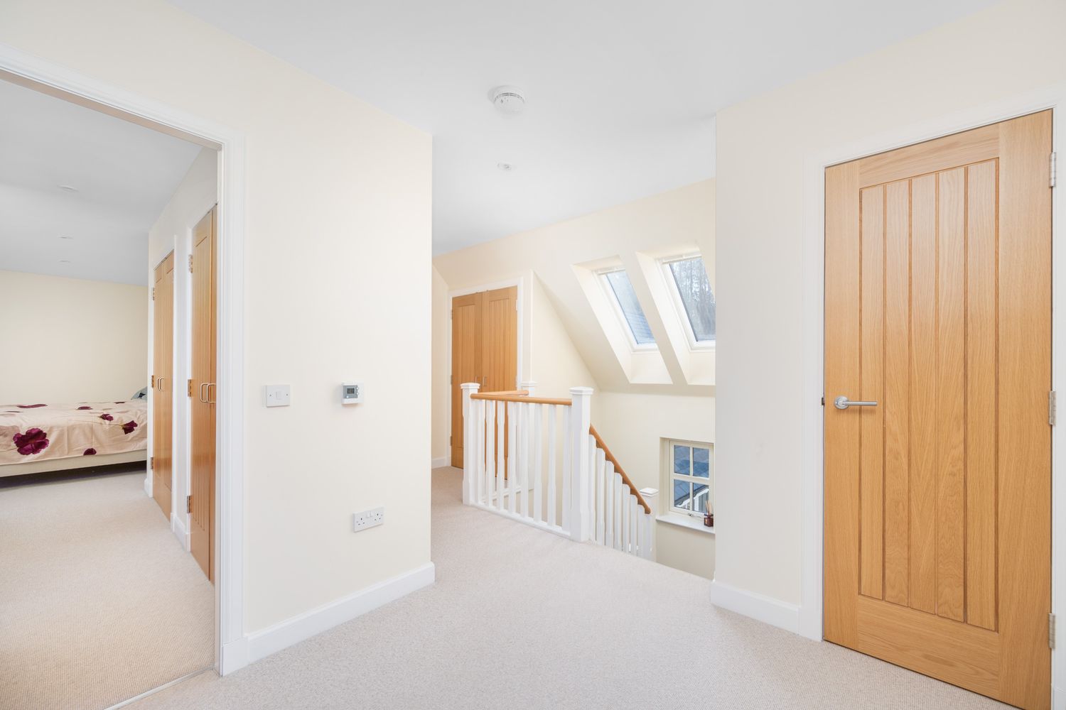 Bright hallway with wooden doors, white walls and carpeted floor leading to skylight.