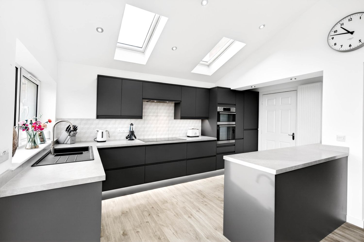 Modern kitchen with white cabinets, black countertops, and sleek appliances featuring a minimalist design and natural lighting.