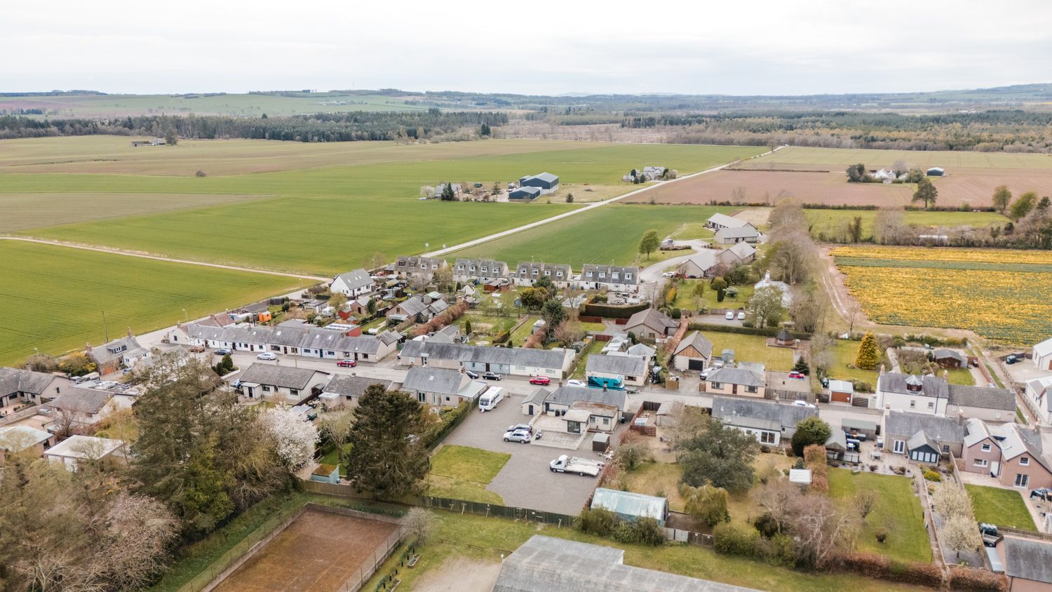 Aerial view of a modern residential subdivision surrounded by green farmland and countryside on a sunny day.