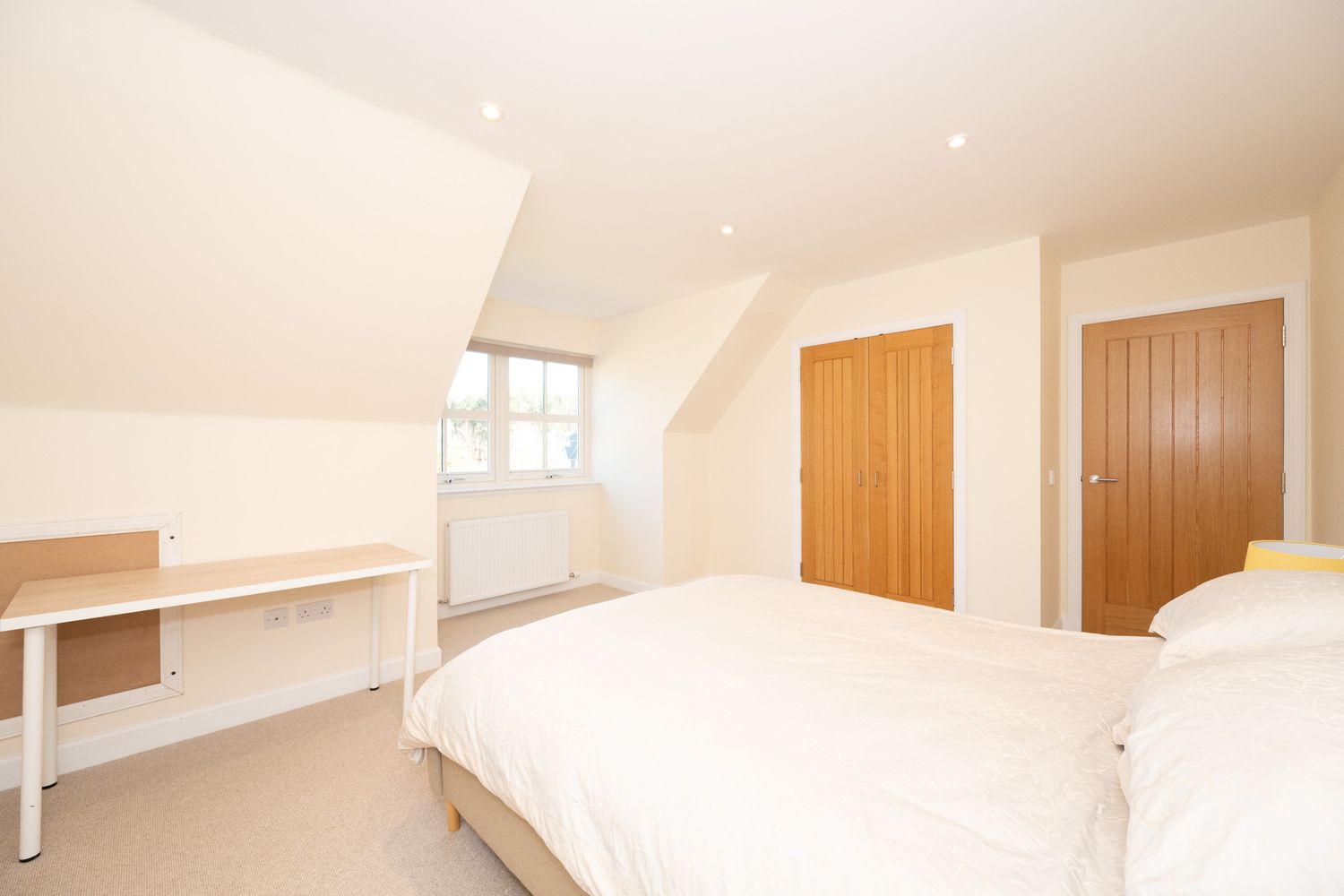A bright and airy attic bedroom with white walls, wooden doors, built-in shelving and a comfortable white bed.