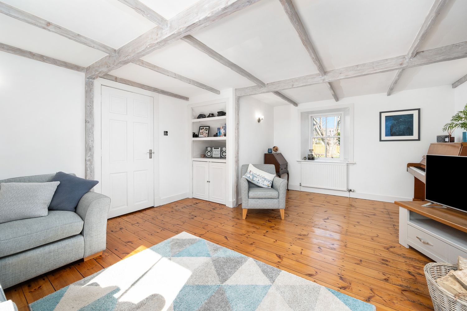 Bright and airy living room with white vaulted ceiling, pine floors, gray couch, and built-in shelving.