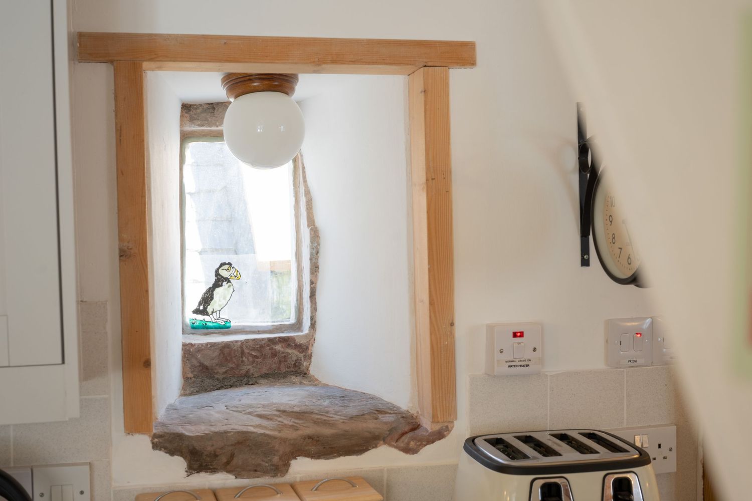 Rustic window frame with decorative bird ornament and white curtains in cottage interior.