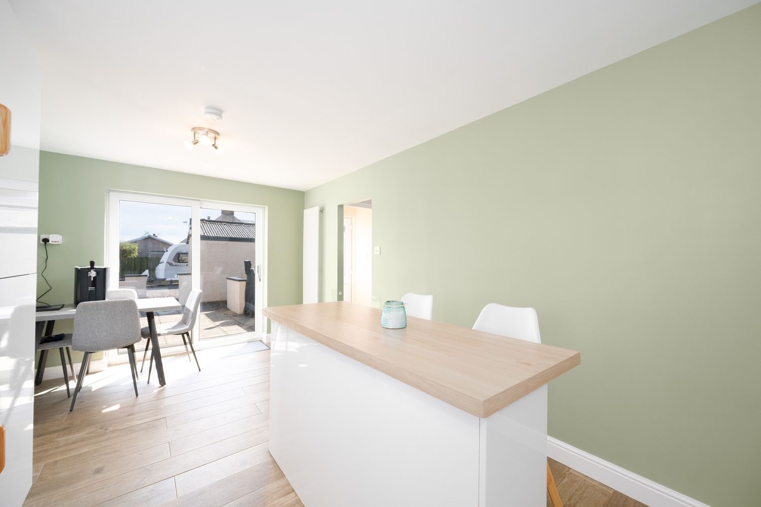Modern open concept living area with sage green accent wall, wood flooring and white kitchen counter divider.