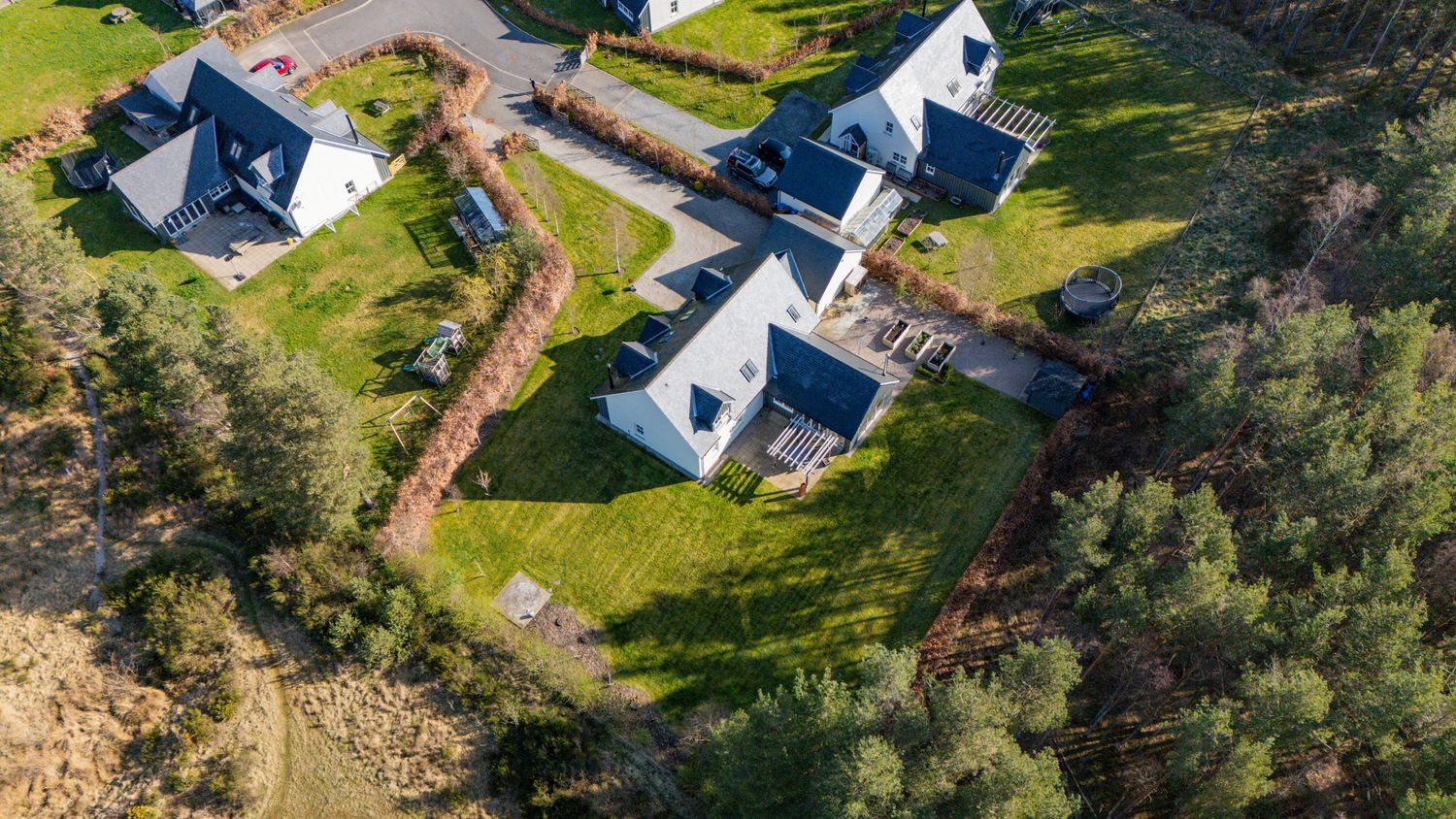 Aerial drone view of modern white houses with dark roofs nestled among green trees on a rocky coastal property.