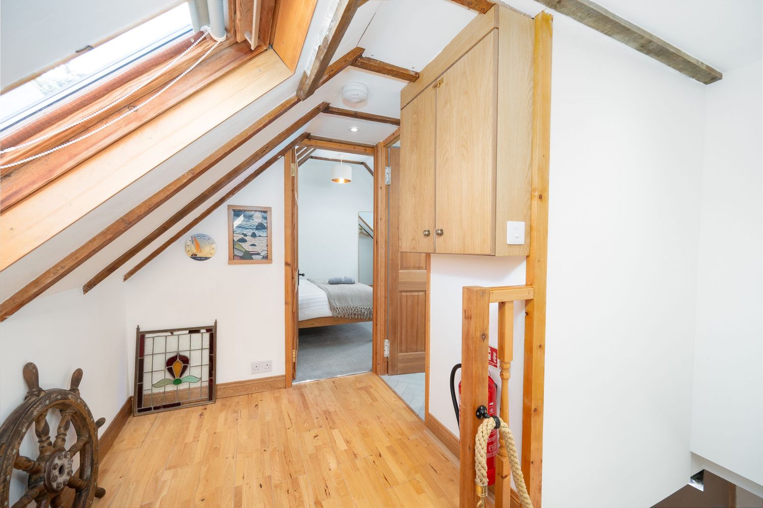 Attic hallway with wooden floors, white walls, nautical decor and a ship's wheel mounted on the wall.