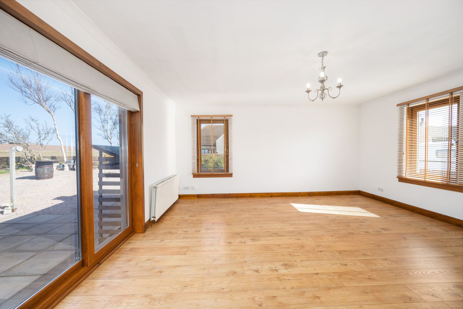 Empty room with hardwood floors, white walls, large glass sliding doors, and wooden window frames in natural light.
