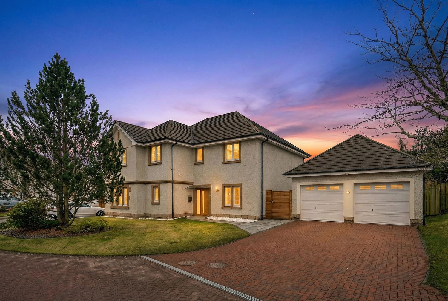 Modern two-story house with attached garage illuminated at sunset with dramatic purple sky.