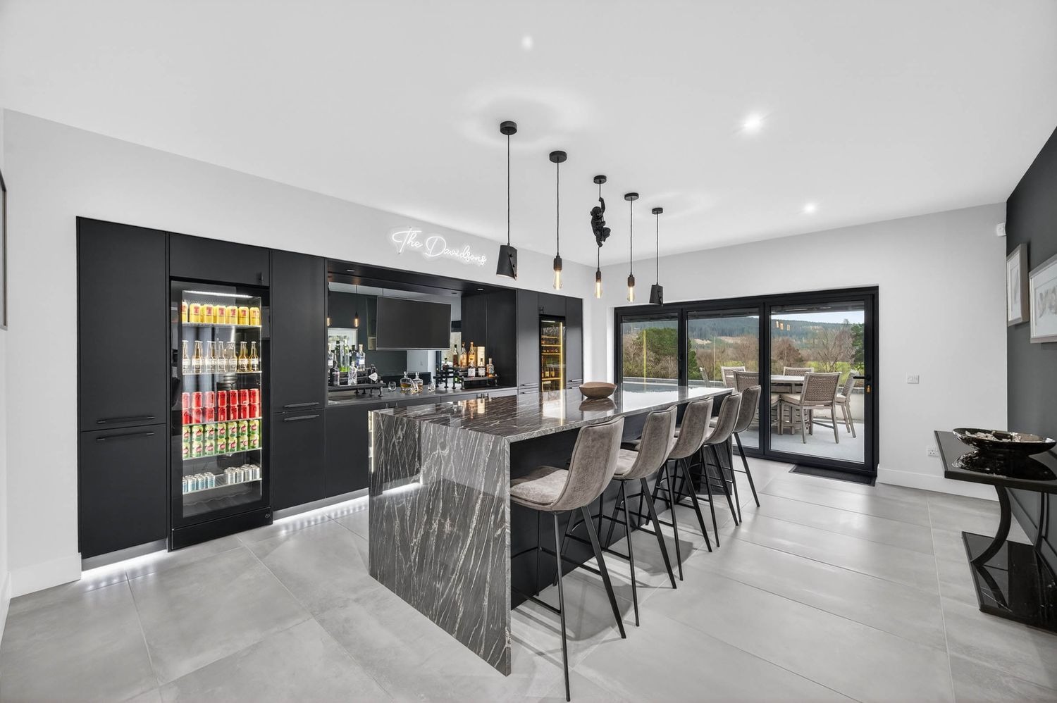 Modern kitchen interior with sleek black cabinets, marble countertops, and bar seating overlooking outdoor views.