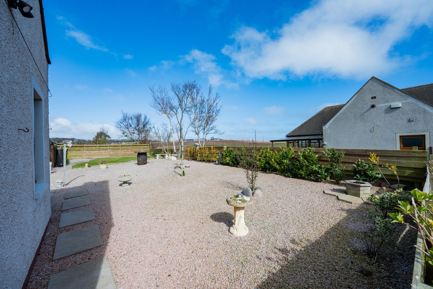 Landscaped gravel garden with white stone pathway and shrubs against blue sky and countryside view.