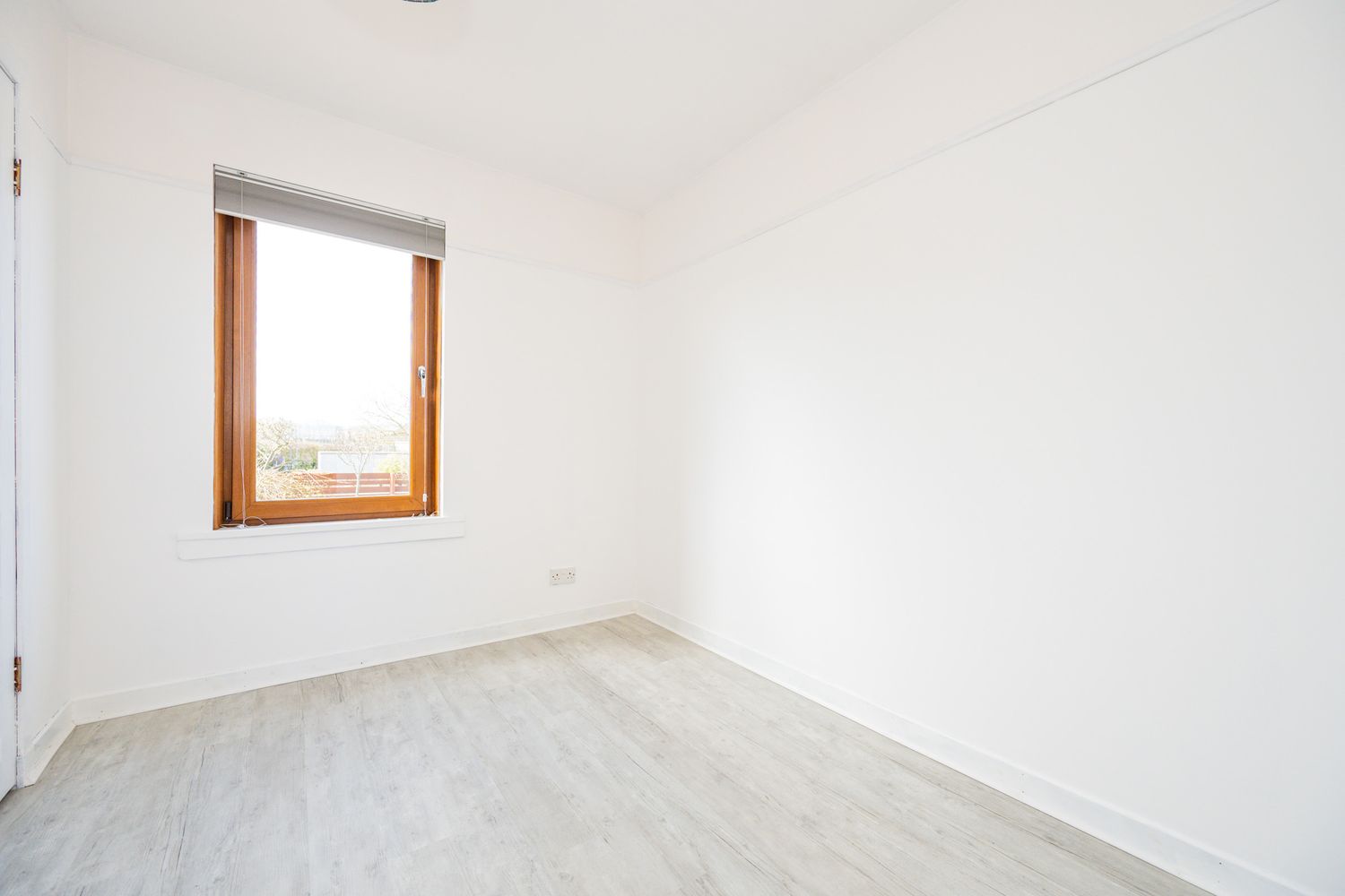 Bright empty bedroom with white walls, wood-framed window and light colored flooring.